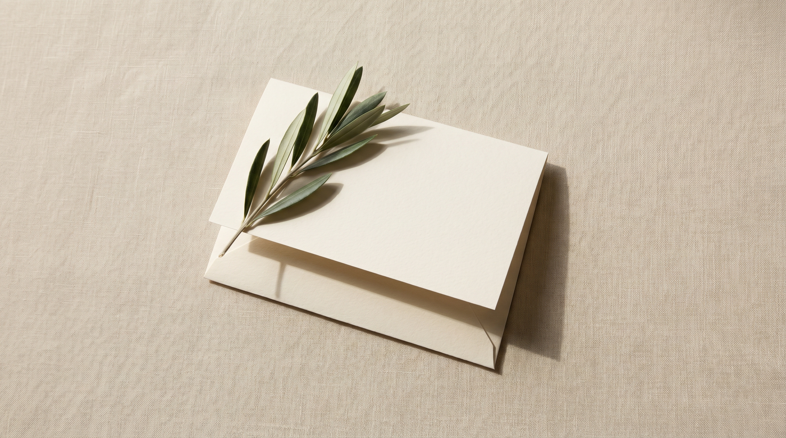 Folded cream paper receipt-shaped card on warm linen with a partially hidden flap and an olive sprig, visual metaphor for hidden cost footnotes