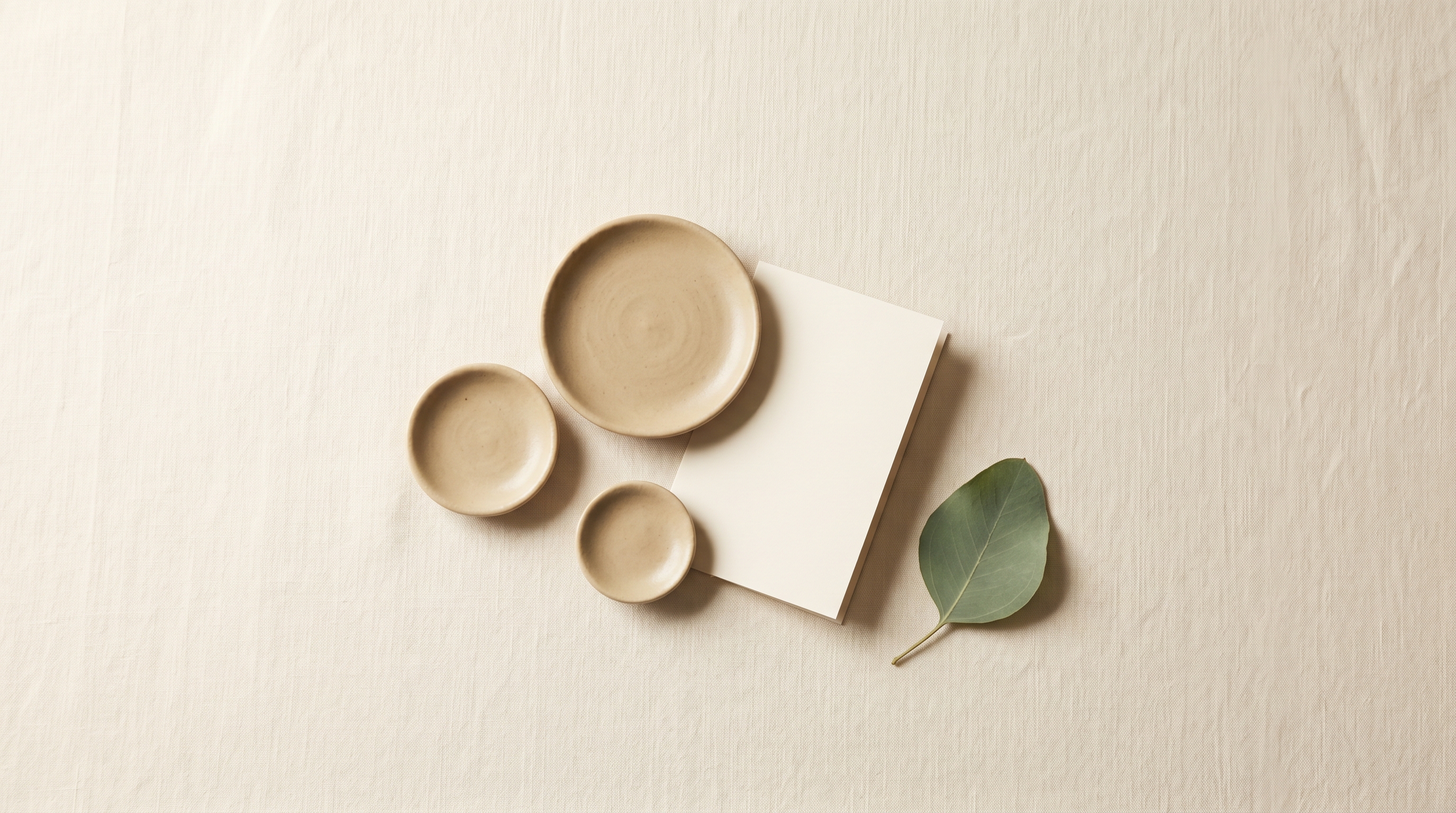Three small bone-ceramic discs of graduated sizes with a folded blank card on linen, abstract tokens of value for a VAT and KRW pricing guide
